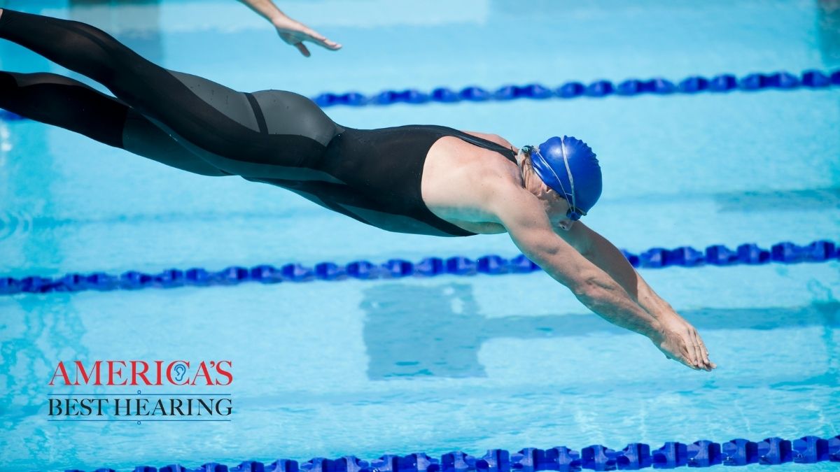 Swimmer wearing a swim cap and goggles diving into a pool, representing activities that can lead to swimmer&rsquo;s ear and the importance of ear care during swimming.
